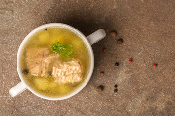 top view of fresh transparent fish soup with sturgeon, potatoes in white plate, decorated black and pink dry peppers, healthy eating, copy space