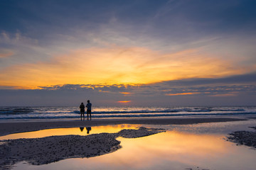 Romantic scene of a couple silhouette of a couple enjoying on the beach watching the sunrise in the morning.