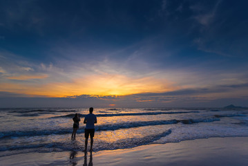 Romantic scene of a couple silhouette of a couple enjoying on the beach watching the sunrise in the morning.