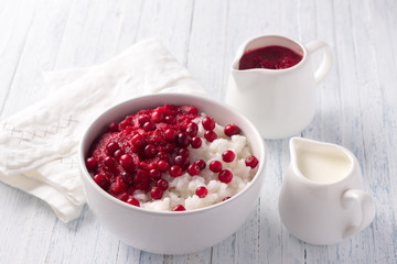 Rice pudding with cranberry jam and fresh cranberries in a white bowl on a light blue background, selective focus. Delicious traditional breakfast