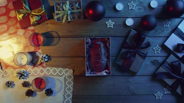 Man opens New Year gift box with real human heart made of plastic inside on decorated wooden table, top down shot