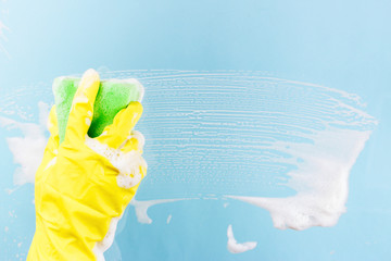 Washing windows and glass. The worker in a yellow glove can stack a sponge with foam on a blue background