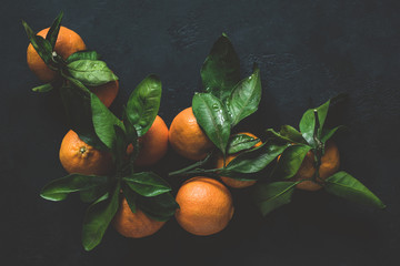 Tangerines with green leaves on dark background. Top view, toned image, moody still life