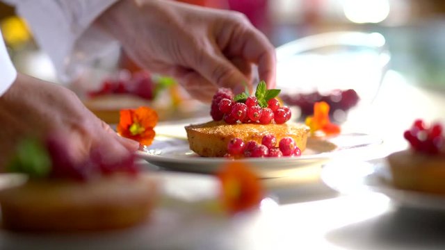 Close-up on the hands of the pastry chef decorating a cake with red currants and a mint leaf before serving.Video