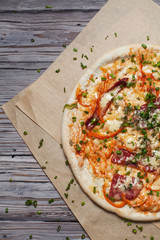 Pizza with a thin crust with cheese, bacon, pepper and herbs on a light wooden background
