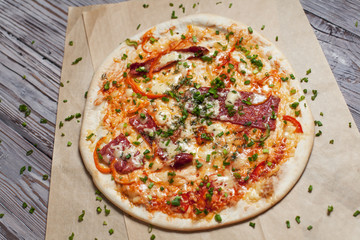 Pizza with a thin crust with cheese, bacon, pepper and herbs on a light wooden background