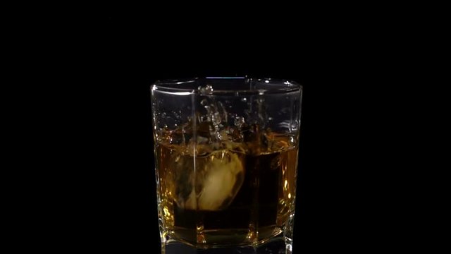 Ice cubes Fall into a glass of Whiskey in Slow Motion on a black background