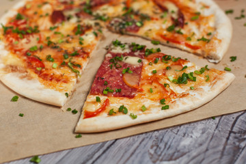 Pizza with a thin crust with cheese, bacon, pepper and herbs on a light wooden background