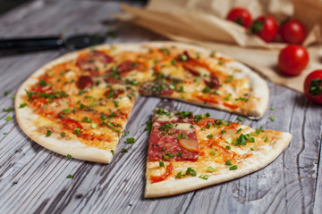 Pizza with a thin crust with cheese, bacon, pepper and herbs on a light wooden background