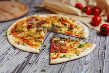 Pizza with a thin crust with cheese, bacon, pepper and herbs on a light wooden background