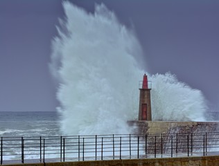 Fototapeta na wymiar Stormy wave over old lighthouse and pier of Viavelez.
