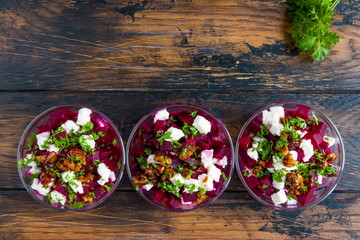 Healthy beet salad with cheese, parsley, walnuts and Greek yogurt in small glass bowls on the rustic wooden table, top view.