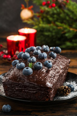 Christmas decoration and sweet chocolate and blueberry cake. Fresh fir-tree brunches on the wooden table and red burning candles.