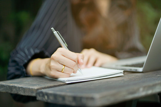 close up woman hand writing something on notebook and playing laptop in free time , lifestyle people concept