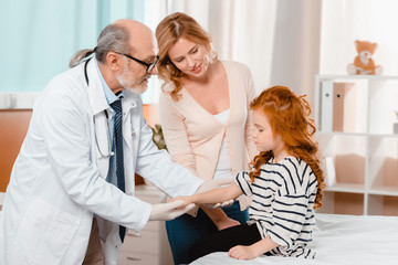 Fototapeta premium portrait of doctor in white coat and medical gloves examining cute little girl during reception in clinic