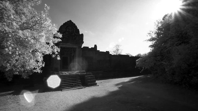 Moving out of the trees to reveal Banteay Srei temple ruins outer wall and getting lens flare from the sun.