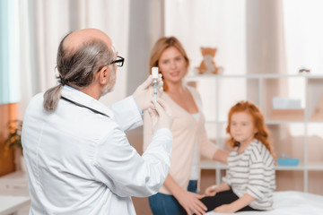 Fototapeta premium lekarz w rękawiczkach medycznych ze strzykawką zamierza zrobić zastrzyk małej dziewczynce w klinice