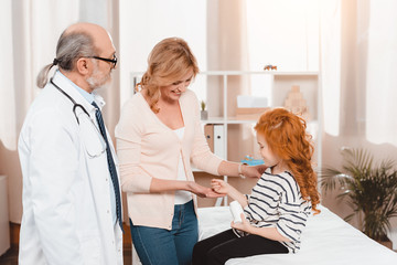 side view of little girl giving pills to mother during doctors reception in clinic