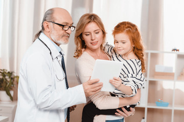 portrait of doctor in white coat, woman and daughter using tablet together in clinic