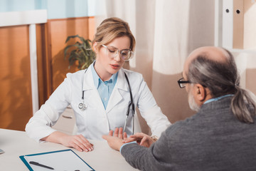 selective focus of focused female doctor in eyeglasses checking patients pulse in clinic