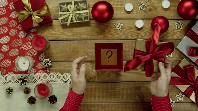 Man opens Christmas present with sticky note with question mark on it, top down shot