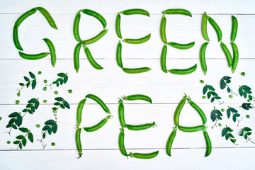 Top view of green pea sign made from fresh green pea pods on white wooden background, copy space. Flat lay. Food natural background