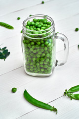 Full glass jar with fresh green peas on white wooden background, copy space. Bio healthy food. Green peas in jar, pods and pea leaves on wooden table