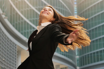 A businesswoman in a business suit, exulted by happiness after finishing the deal, in the background skyscrapers. Concept of: business, technology, economy and work and success