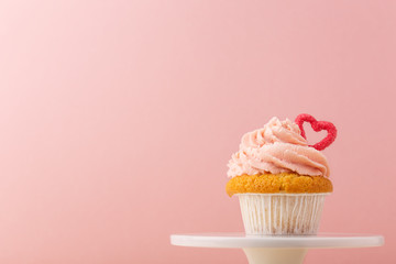 Closeup of small muffin with pin frosting decorated with small heart and composed on cake stand.