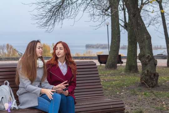  Female teenagers listening to music on smartphone sitting on the bench in an autumn city park