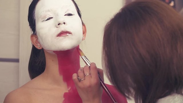 Face art. Makeup artist painting on the model's neck and shoulders with red color foudation.