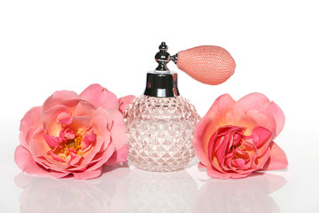 Obraz na płótnie Canvas Aroma of roses. Perfume with the scent of a rose in a glass rose bottle and two pink roses on a white background. Eau de toilette with a rose scent