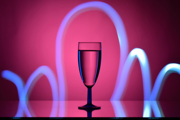 Wine in a glass goblet on a pink background with a gradient spot and stream of light on dark tones 
