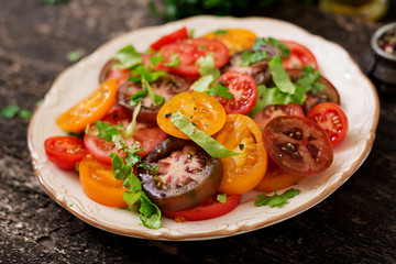 Summer salad of tomatoes of different colors with green herbs and pepper.