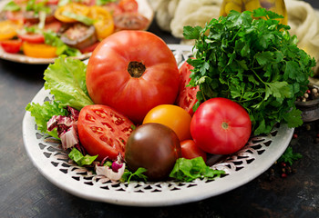 Tomatoes of different colors with green herbs in a bowl on a black background