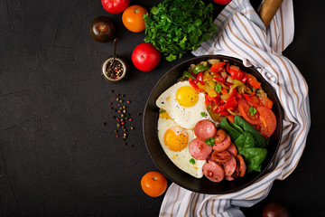 Breakfast. Fried eggs with sausage and vegetables in a frying pan on a black background in rustic style. Top view © timolina