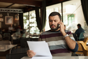 Confused man talking on phone and looking at papers