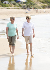 two lovely senior mature retired women on their 60s having fun enjoying together happy walking on the beach smiling playful