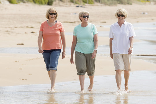 lovely group of three senior mature retired women on their 60s having fun enjoying together happy walking on the beach smiling playful
