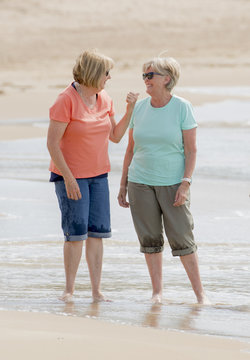 two lovely senior mature retired women on their 60s having fun enjoying together happy walking on the beach smiling playful