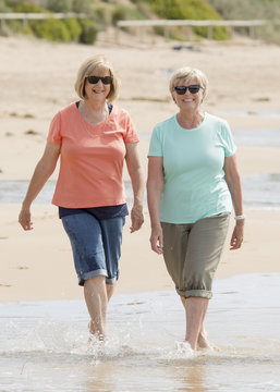 two lovely senior mature retired women on their 60s having fun enjoying together happy walking on the beach smiling playful