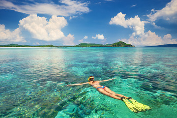 Woman snorkeling in clear tropical waters on a background of exotic islands. - obrazy, fototapety, plakaty