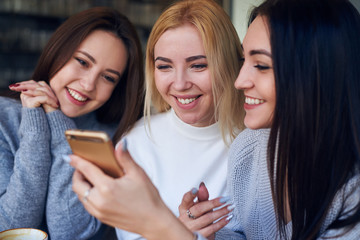 Three young beautiful women using mobile phone at cafe