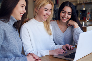 Three women having good time while sitting around a laptop at cafe
