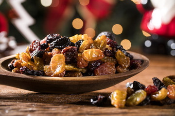 Raisins into a bowl on rustic old wooden table with christmas background.