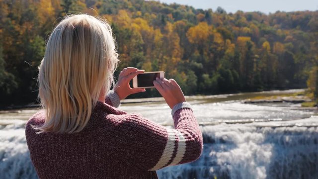 A woman is taking a picture of a waterfall in Letchworth State Park.
