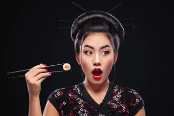 Foto op Plexiglas Verrast Aziatische vrouw sushi eten en rollen op een zwarte achtergrond. © Mike Orlov