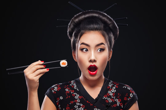 Surprised Asian woman eating sushi and rolls on a black background.