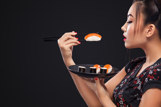 Asian woman eating sushi and rolls on a black background.