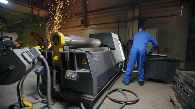 Factory workman putting metal plate in modern turning machine for bending